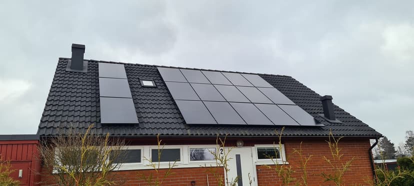 Svensk villa med svarta solpaneler på taket under molnig himmel