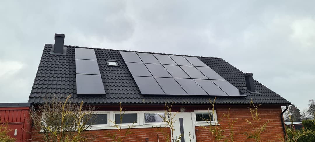 Svensk villa med svarta solpaneler på taket under molnig himmel
