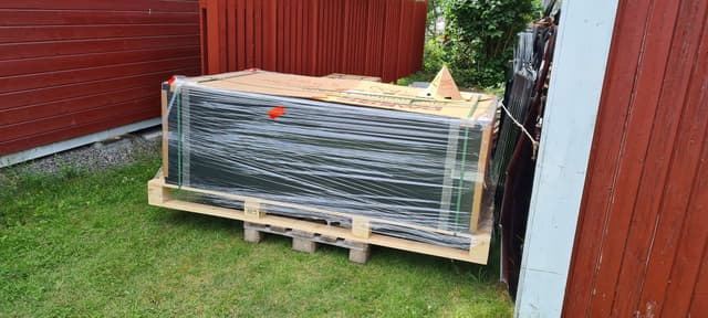 Plastad pall med levererade solpaneler vid röd ladugårdsvägg
